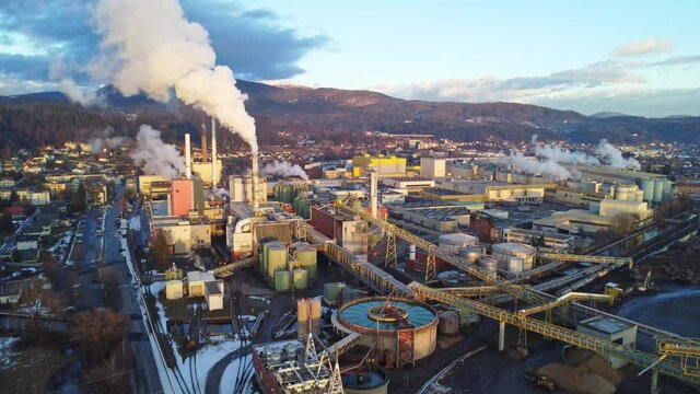 Aerial view of a huge paper factory facility in Austria during sunset. Lots of steam coming out of chimneys and pollute the air. 