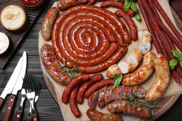 Fototapeta Different delicious sausages with herbs and sauces on black wooden table, flat lay. Assortment of beer snacks obraz