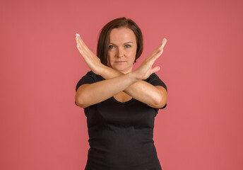 woman in black T-shirt with her arms crossed in front of her, X sign, pink background
