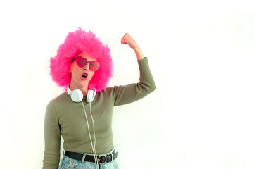 Woman wearing a pink wig and heart shaped glasses using headphones. 