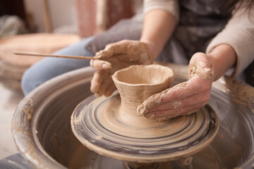 Fototapeta na wymiar Cropped close up of female hands on potters wheel, shaping clay bowl, copy space