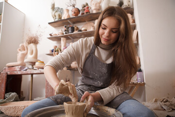 Low angle shot of beautiful woman enjoying working with clay on a potters wheel at crafts studio