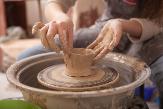 Close up cropped shot of female hands shaping clay on potters wheel