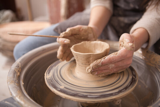 Cropped close up of female hands on potters wheel, shaping clay bowl, copy space