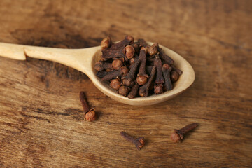 Aromatic dry cloves and spoon on wooden table, closeup