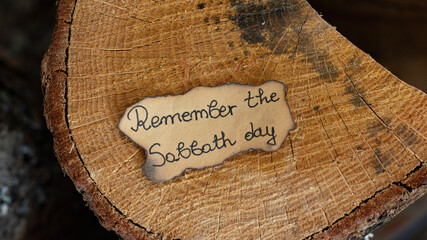 Remember the Sabbath Day text quote handwritten on old paper on an oak wooden log. Top overhead...