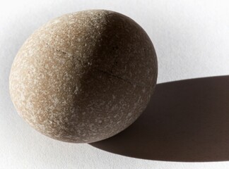 Smooth oval, nearly round pebble illuminated from the left, casting a shadow on the paper mat