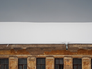 The roof of the vintage house is covered with snow. A snow-covered roof of a old house.