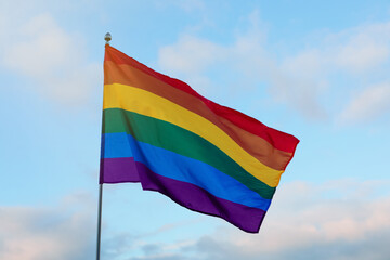 Bright LGBT flag against blue sky with clouds