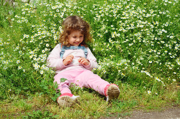 Little girl sitting in a green summer garden with green grass and daisy flowers 