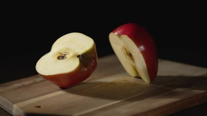 Slow motion. A ripe red apple falls into two pieces on a black background. Close-up shooting.