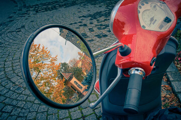 Urban red scooter is parked, reflection of the old city in the mirror 