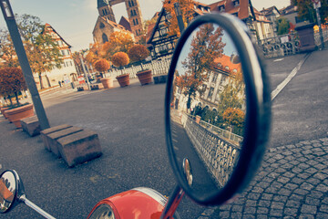Urban red scooter is parked, reflection of the old city in the mirror 