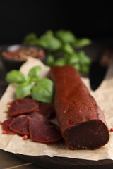 Delicious dry-cured beef basturma with basil and peppercorns on wooden table, closeup