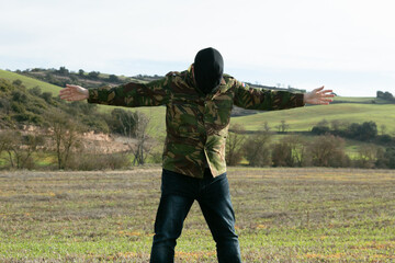 Soldado con camisa en  camuflaje y pasamontaña en color negro con las manos en forma de detención, irreconocible
