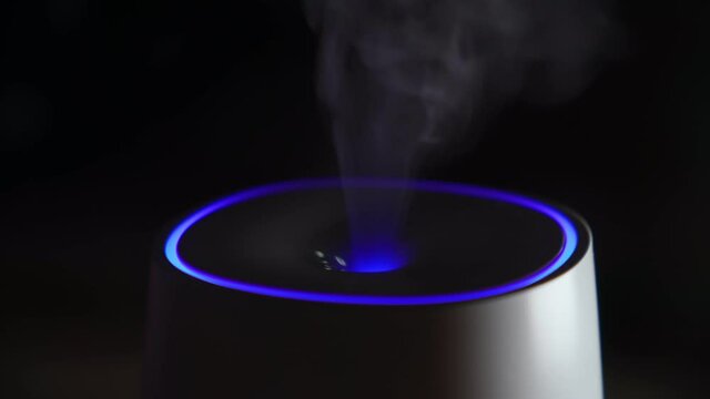 Essential oil diffuser releases smoke on a dark background. Selective focus
