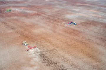 Spring sowing works. Aerial view of tractors working in the field. In parallel, seed sowing and soil harrowing are carried out. Shooting from a drone.
