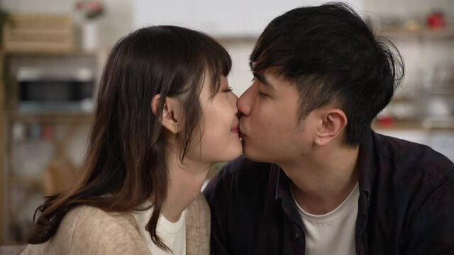 slow motion with closeup of asian romantic young couple gently kissing on lips at home. the woman looking at her boyfriend with a smile