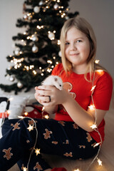 A teenage girl in a red festive T-shirt sitting with a hamster in her hands at the Christmas tree