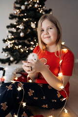 A teenage girl in a red festive T-shirt sitting with a hamster in her hands at the Christmas tree