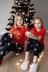 Teenage sisters in red holiday T-shirts sitting at the Christmas tree and celebrating the New Year