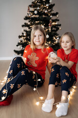 Teenage sisters in red holiday T-shirts sitting at the Christmas tree and celebrating the New Year