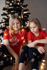 Teenage sisters in red holiday T-shirts sitting at the Christmas tree and celebrating the New Year