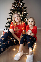 Teenage sisters in red holiday T-shirts sitting at the Christmas tree and celebrating the New Year