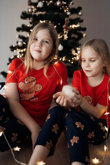 Teenage sisters in red holiday T-shirts sitting at the Christmas tree and celebrating the New Year