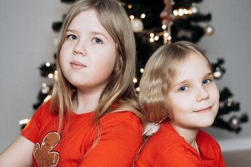 Teenage sisters in red holiday T-shirts sitting at the Christmas tree and celebrating the New Year