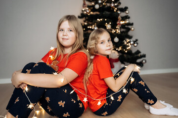 Teenage sisters in red holiday T-shirts sitting at the Christmas tree and celebrating the New Year