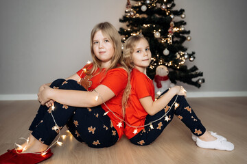 Teenage sisters in red holiday T-shirts sitting at the Christmas tree and celebrating the New Year