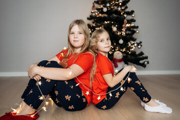 Teenage sisters in red holiday T-shirts sitting at the Christmas tree and celebrating the New Year