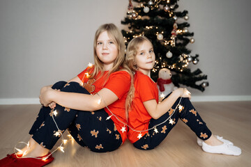 Teenage sisters in red holiday T-shirts sitting at the Christmas tree and celebrating the New Year