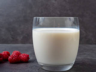 A glass of milk and raspberries on a gray table.