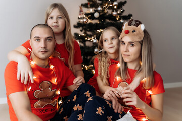 A family in red holiday T-shirts sitting at the Christmas tree and celebrating the New Year