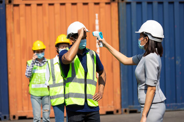 female manager measures temperature with a thermometer for employees before entering a container yard. import and export concept. Professional engineering team.