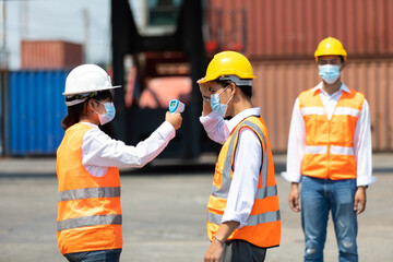 female manager measures temperature with a thermometer for employees before entering a container yard. import and export concept. Professional engineering team.