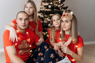A family in red holiday T-shirts sitting at the Christmas tree and celebrating the New Year
