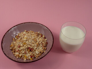 Muesli in a pink cup and a glass of milk on a pink table. Muesli on a pink background.