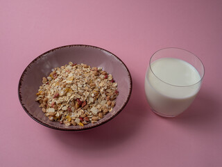 Muesli in a pink cup and a glass of milk on a pink table. Muesli on a pink background.