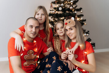 A family in red holiday T-shirts sitting at the Christmas tree and celebrating the New Year