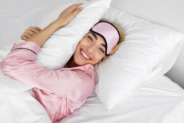 Happy young pretty blonde female in pink pajamas and sleep mask wake up