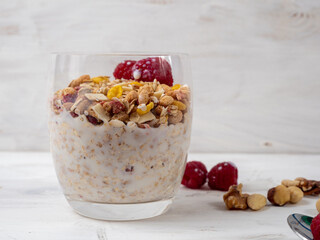 Muesli in a glass glass and berries on a white table. Muesli on a wooden white background.