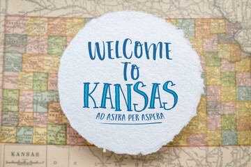 welcome to Kansas, ad astra per aspera - handwriting on a circular sheet of rough handmade paper floating over vintage defocused map of Kansas, hospitality and travel concept