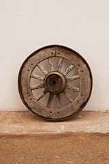 Fototapeta na wymiar Isolated old wooden wagon wheel leaning against a white wall