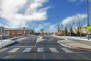 Empty roadway intersection, winter daytime, traffic signage, traffic lights and crosswalk markings, blue sky with clouds and buildings in background, nobody