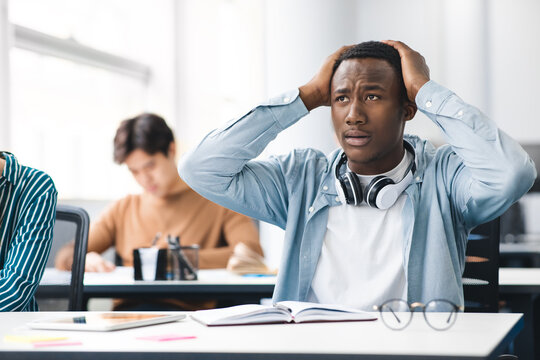 Black male student grabbing head sitting at desk in class