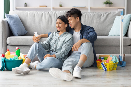 Cute asian couple with cellphone having break after cleaning