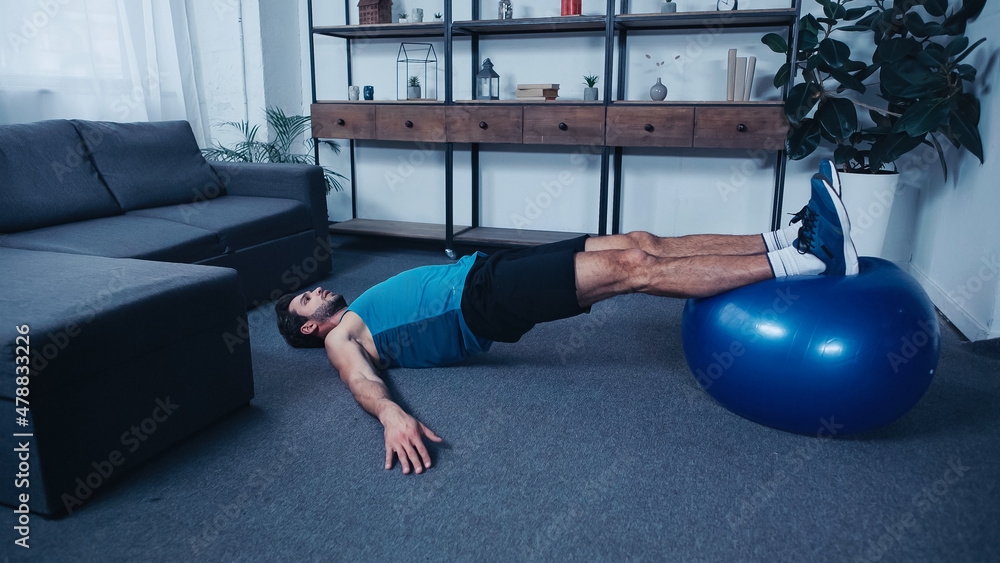 Wall mural young sportsman training on blue fitness ball at home